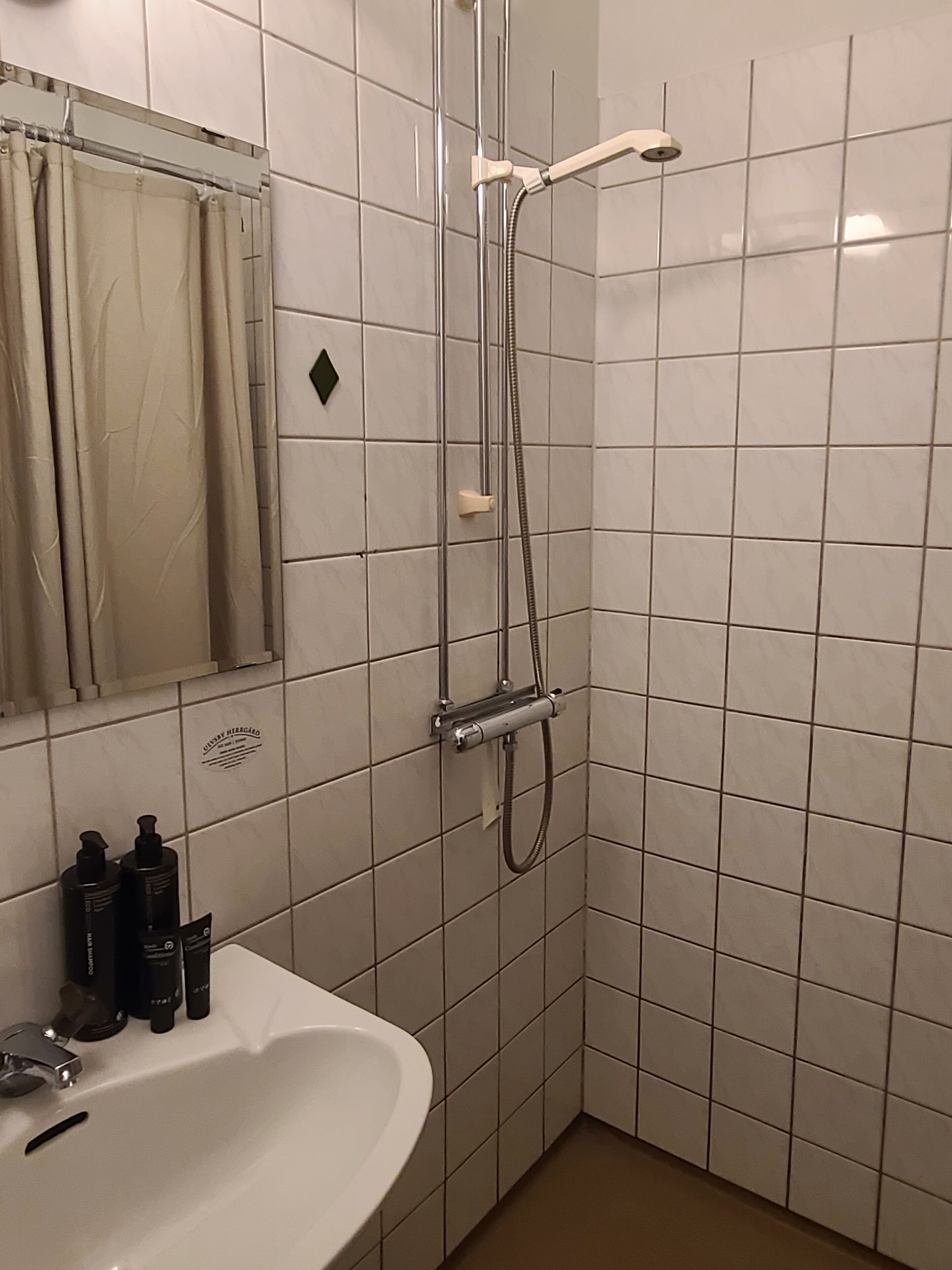 Un baño con un lavabo blanco, un espejo y una ducha con cabezal de ducha de mano.