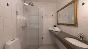 A modern bathroom with a glass shower enclosure, a sink with a marble countertop, and a large mirror with a gold frame.