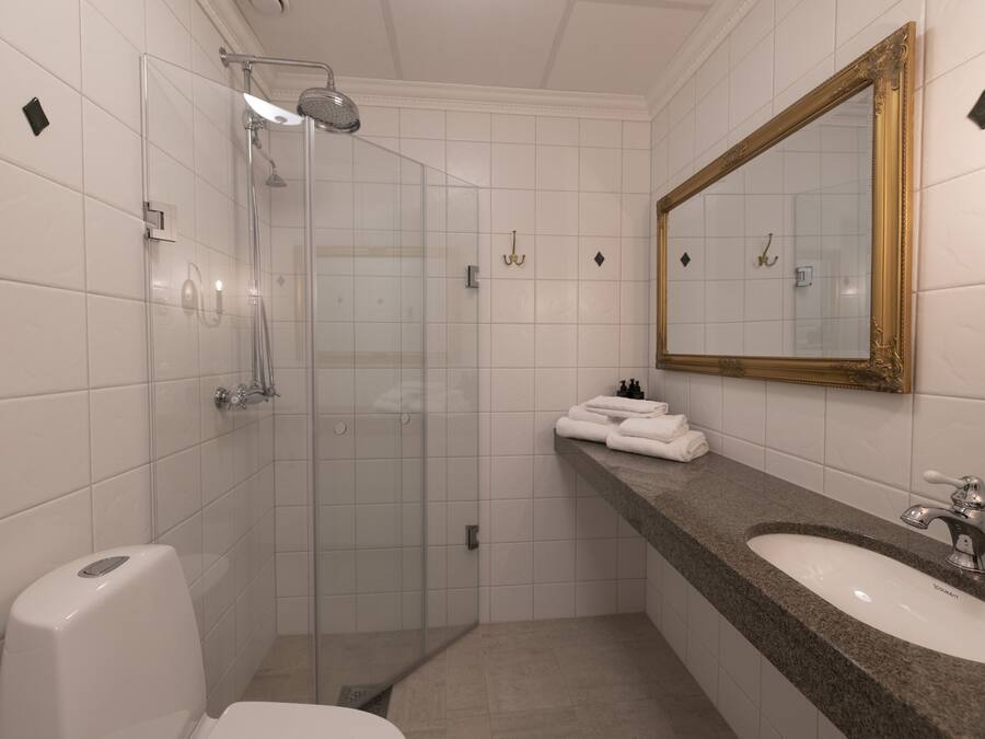 A modern bathroom with a glass shower enclosure, a sink with a marble countertop, and a large mirror with a gold frame.