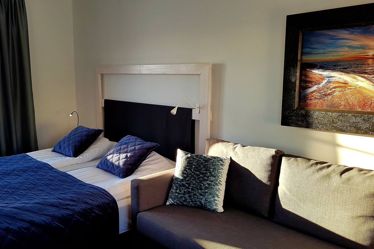 A bedroom with a bed, a sofa, a painting, and a window with curtains.