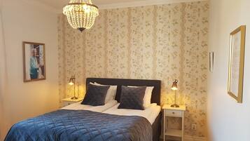 Une chambre à coucher avec un grand lit, deux tables de chevet avec des lampes, un papier peint à motifs floraux et un lustre.