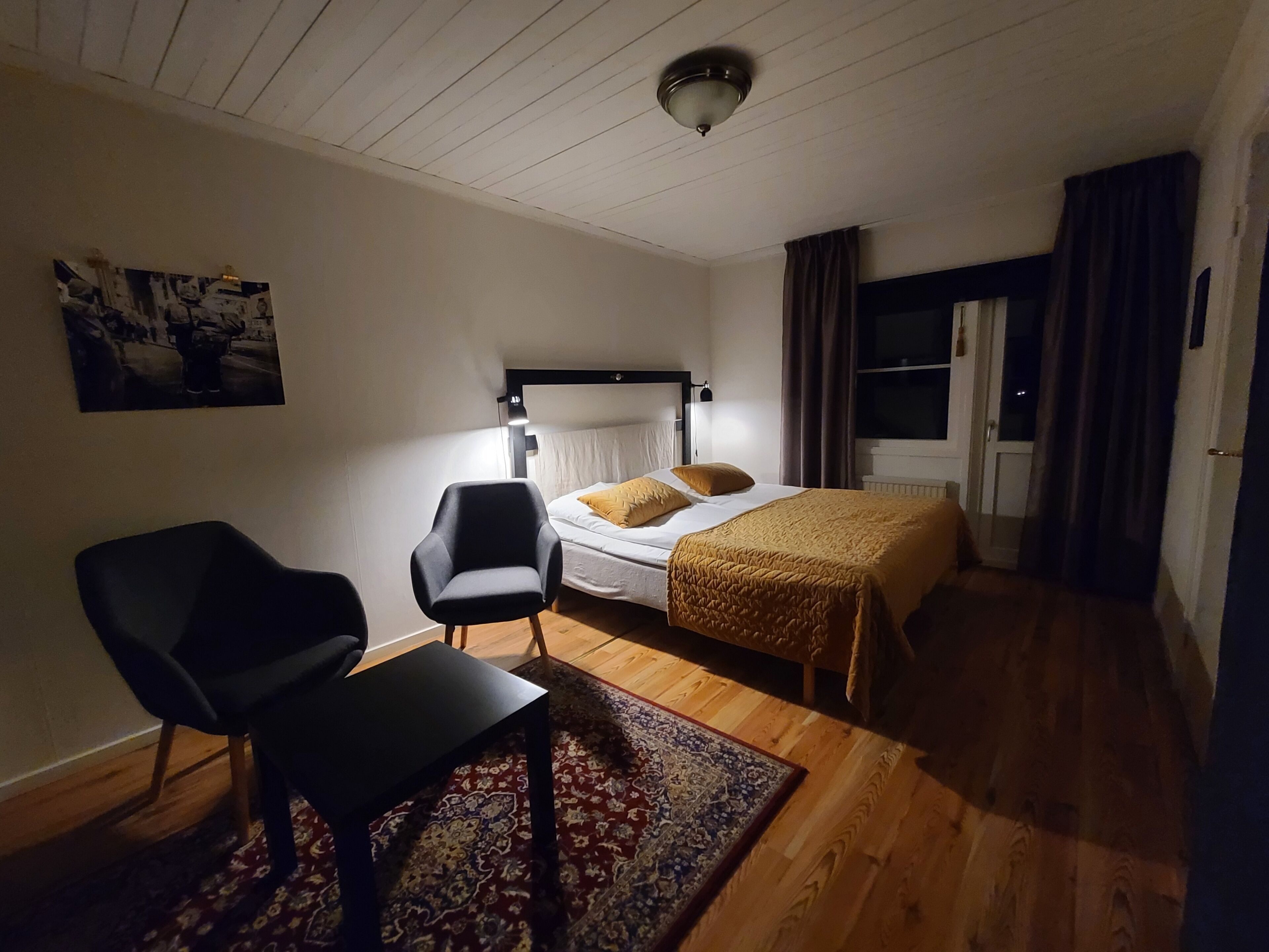 A bedroom with a bed, a chair, a desk, a rug, a ceiling fan, and a window with curtains.