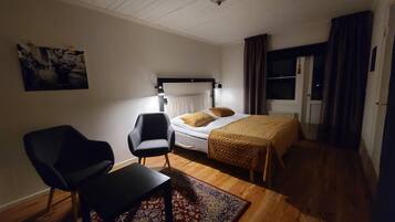 A bedroom with a bed, a chair, a desk, a rug, a ceiling fan, and a window with curtains.