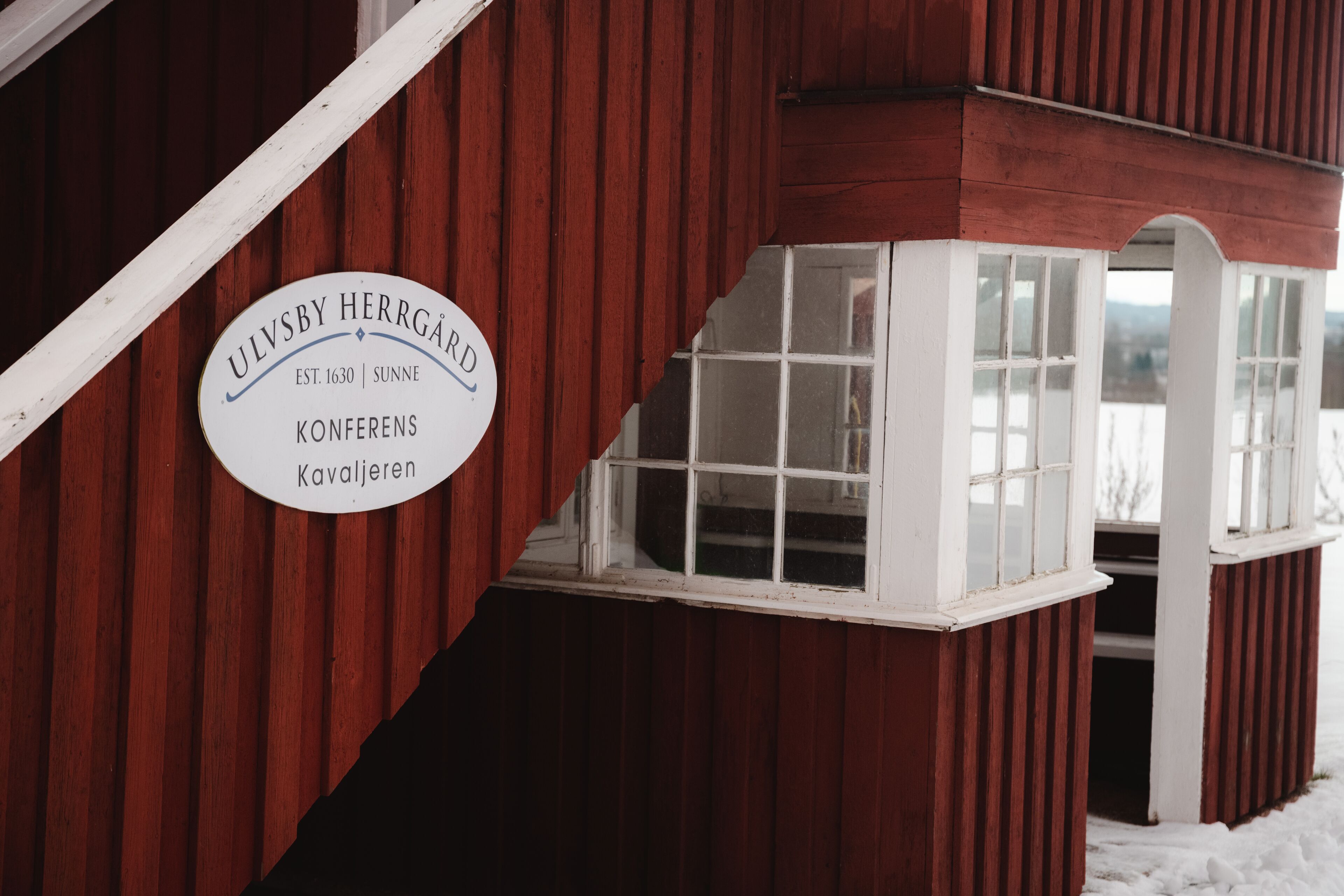 En byggnad av trä med en skylt som lyder: ”ULVSBY HERRGÅRD – KONFERENS – KAVALJEREN”.