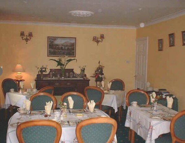 Comedor con mesas dispuestas para cuatro, sillas, una araña y luces de pared, además de un cuadro sobre las mesas.