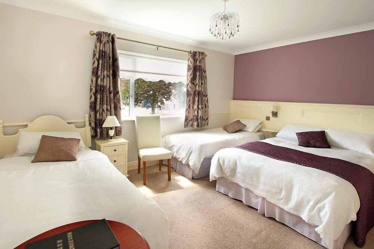 A hotel room with two beds, a desk, a chair, and a window with curtains.