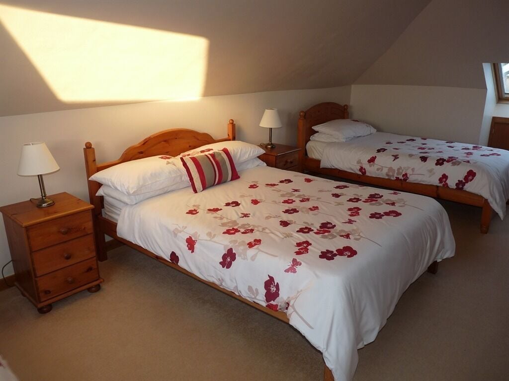Un dormitorio con dos camas individuales, cabeceros de madera, mesitas de noche con lámparas y suelo alfombrado.