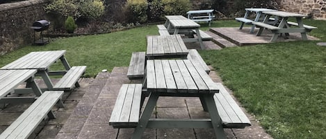 En have med picnicborde placeret på stenfliser.