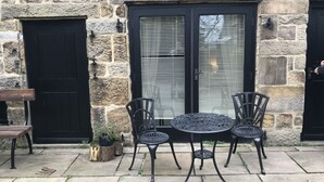 A stone building with a black door and windows with blinds. There is a round table with chairs and a bench outside. - Duke of Wellington (Matlock)