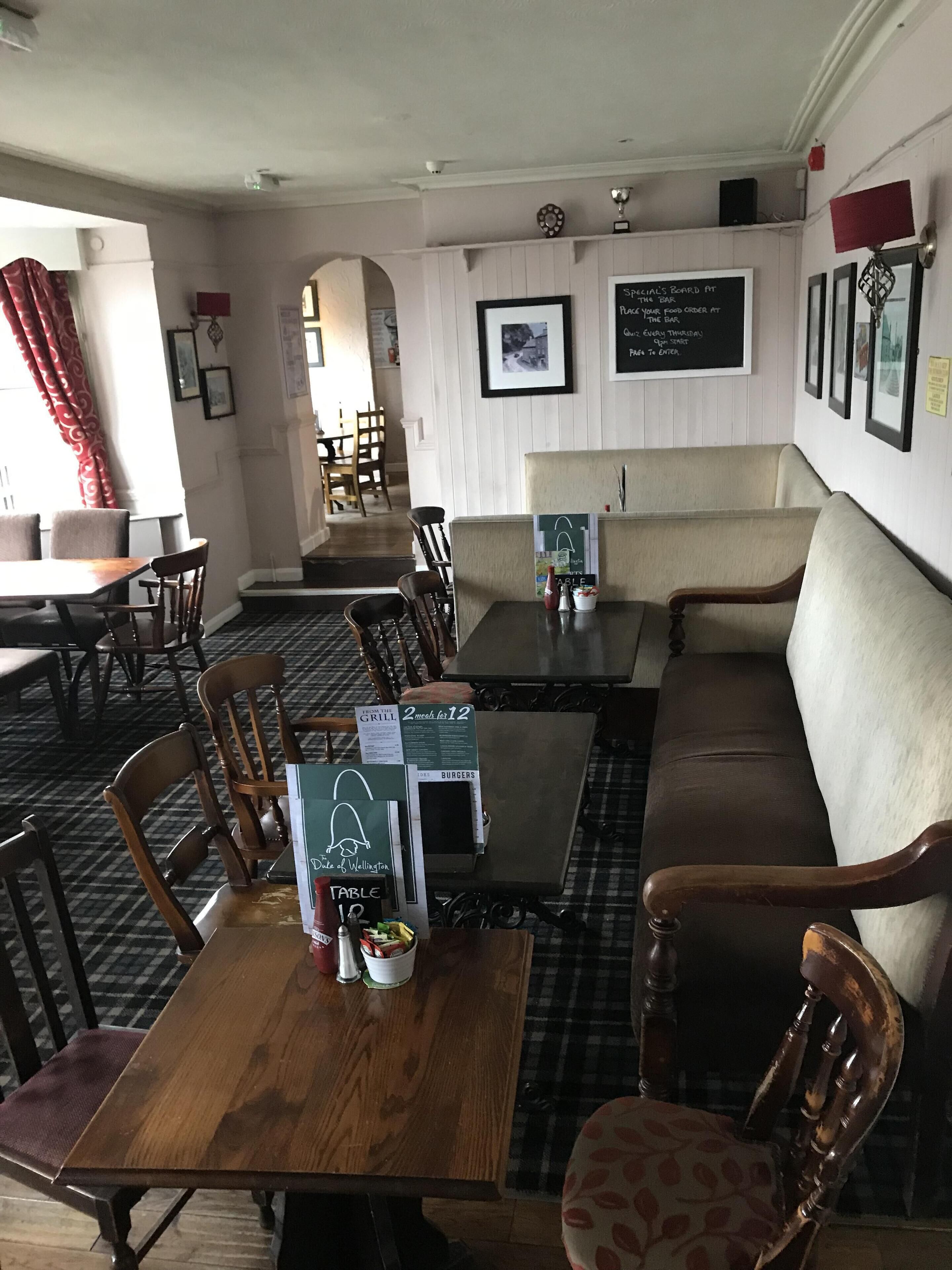 A restaurant with a bar area, wooden tables, and a sofa. There are signs indicating menu items and specials.