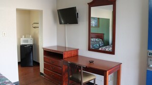 A hotel room with a wooden desk, a flat-screen TV, a microwave, and a mirror.