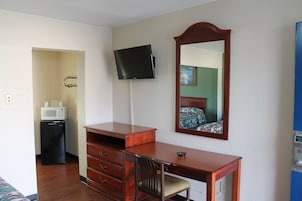 Habitación de hotel con escritorio de madera, televisor de pantalla plana, microondas y espejo.