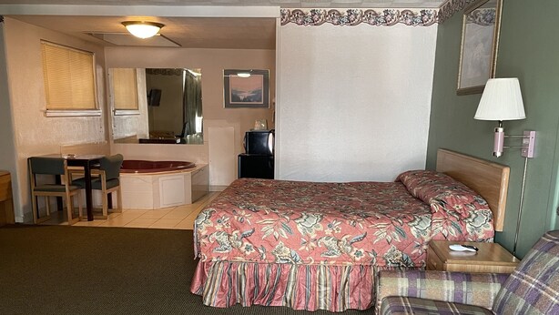 A hotel room with a bed, a sofa, a desk with a chair, a mirror, and a lamp.