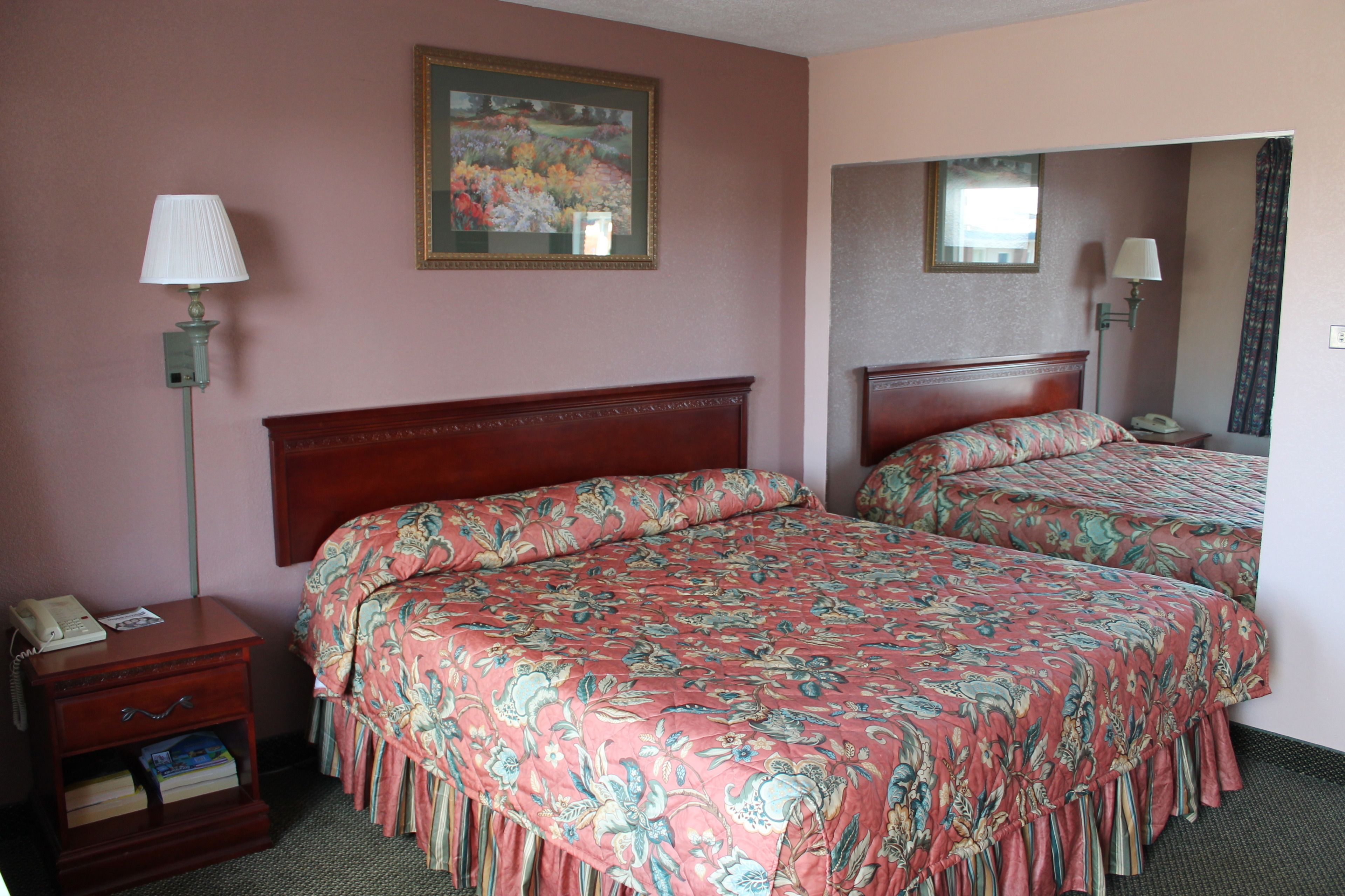 A hotel room with two beds, a nightstand with a telephone, a lamp, and a painting on the wall.
