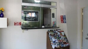A reception area with a glass window, a 'Ring Bell for Service' sign, and a display of magazines.
