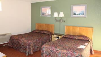 Two single beds with matching headboards and patterned bedspreads, a nightstand with wall-mounted lamps, and a window with an outdoor view.