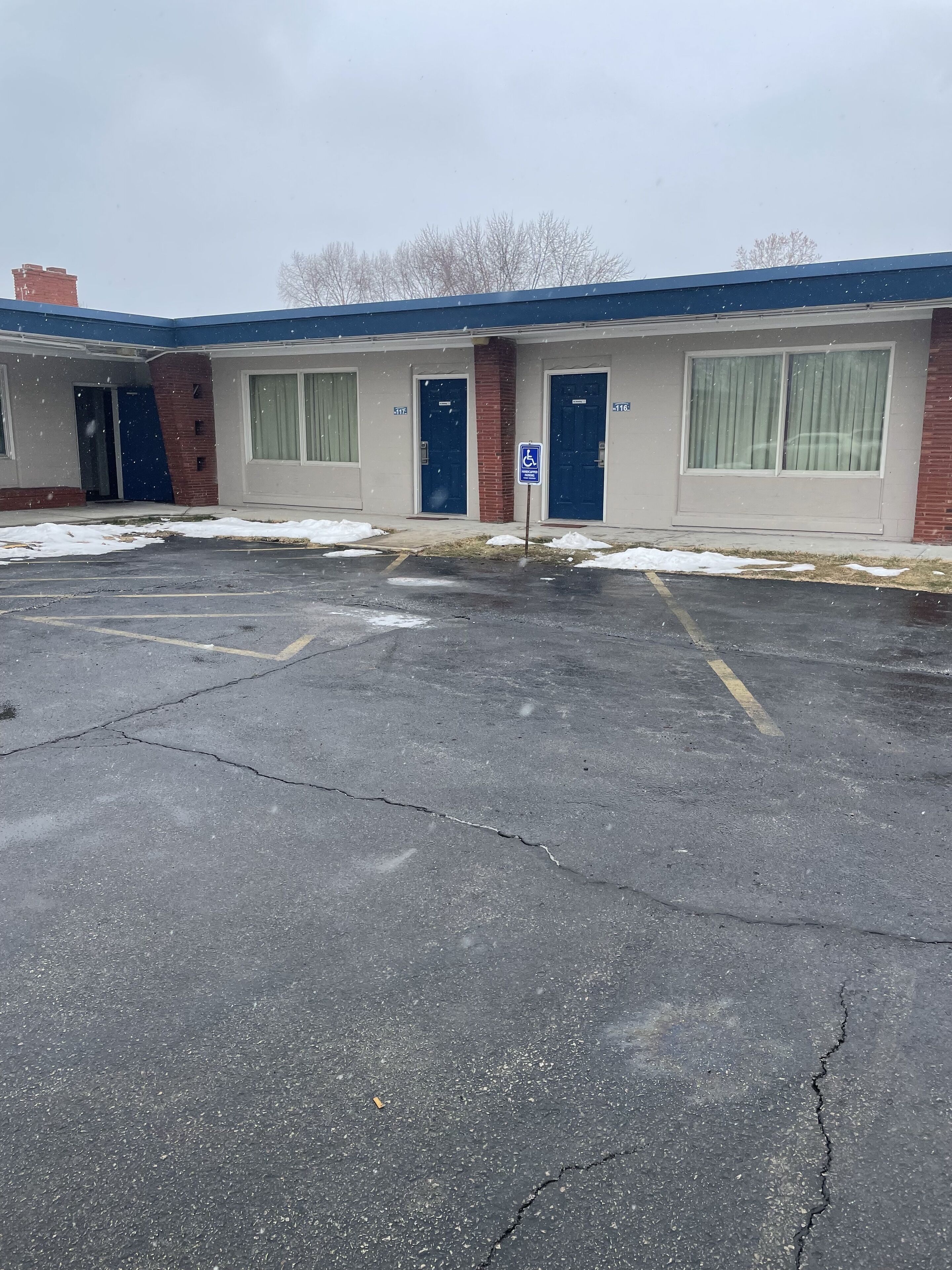 Un edificio con varias entradas, un letrero de accesibilidad para personas con discapacidad y un estacionamiento cubierto de nieve.