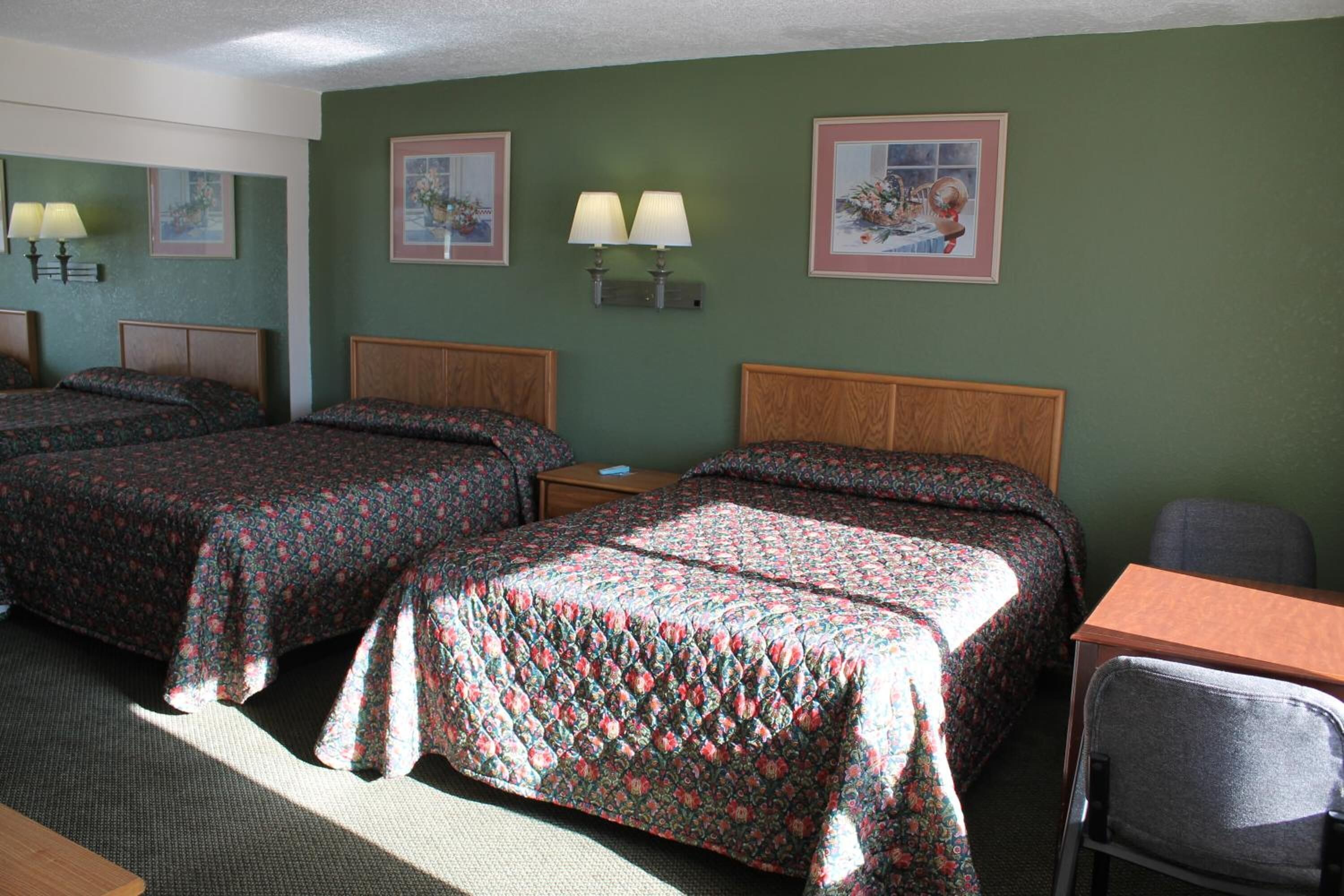 A hotel room with two beds, a desk, and a chair. There are wall-mounted lamps and framed pictures on the walls.
