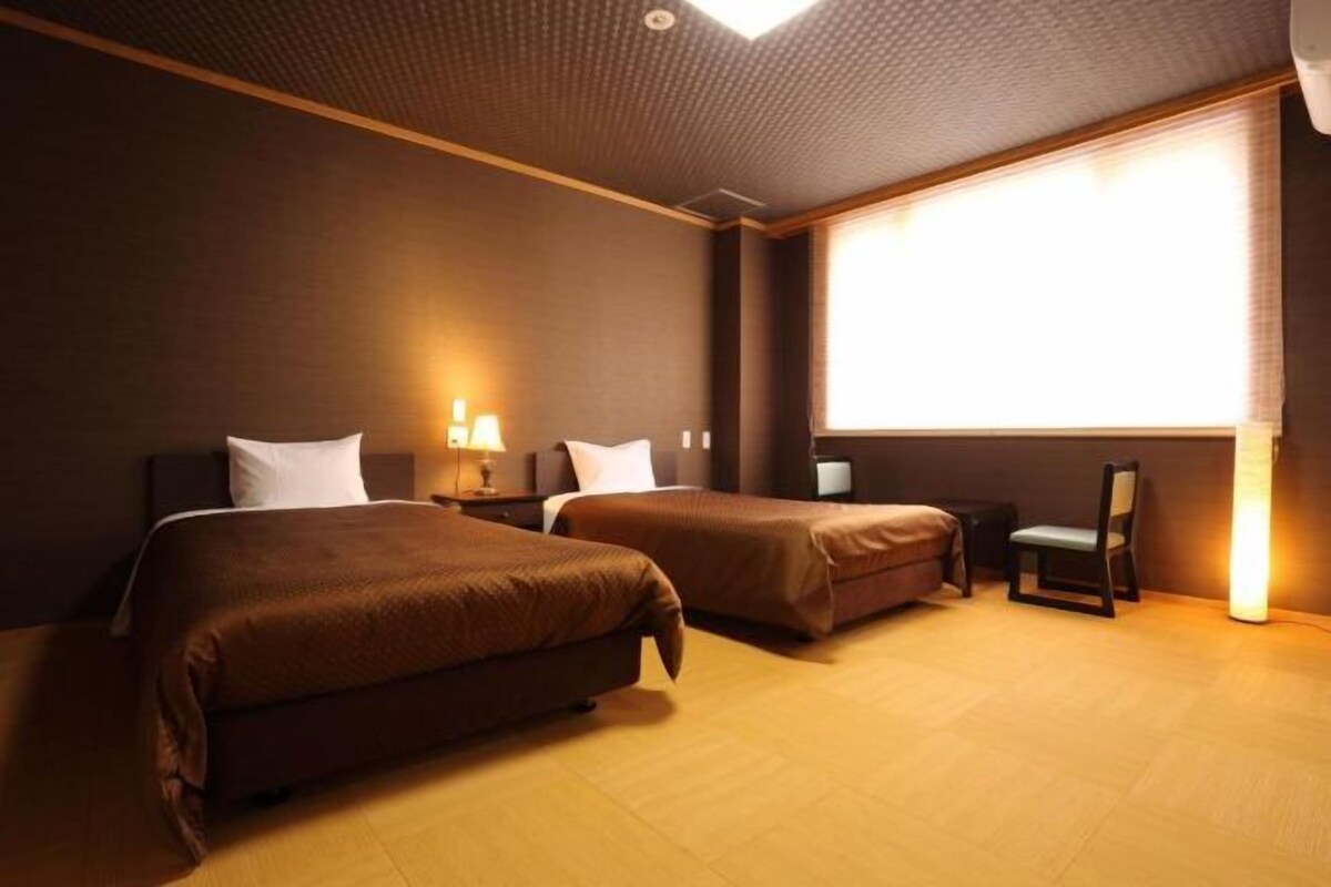 A hotel room with two beds, a chair, a desk, and a large window.