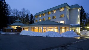 A hotel with multiple floors, a covered lobby, and snow accumulation around the entrance. - Hotel Oak Forest (Hakuba)