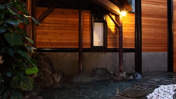 A wooden structure with a stone pathway leading to a water feature, surrounded by rocks and plants.