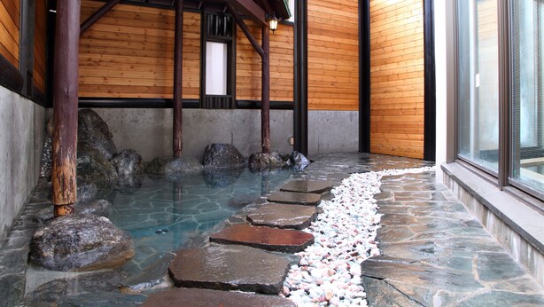 A stone pathway leading to a hot spring area with wooden walls and a wooden roof structure. - Hotel Oak Forest (Hakuba)