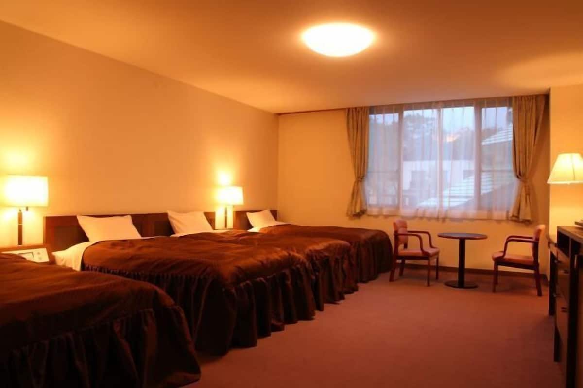 A hotel room with two beds, a small table, two chairs, and a window with curtains.