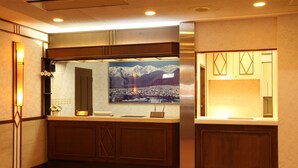A hotel reception area with a wooden counter, a framed picture of mountains, and a cash register. - Hotel Oak Forest (Hakuba)