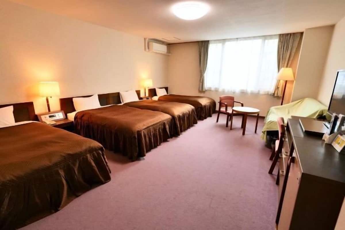 A hotel room with three beds, a desk, a chair, and a television.