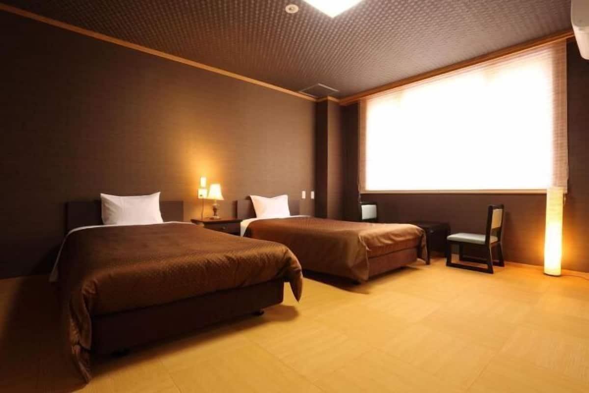 A hotel room with two beds, a chair, a desk, and a large window.