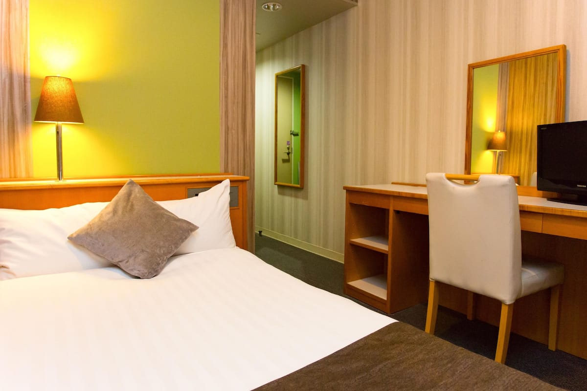 Une chambre d’hôtel équipée d’un lit, d’un bureau, d’une chaise, d’une télévision et d’un miroir.