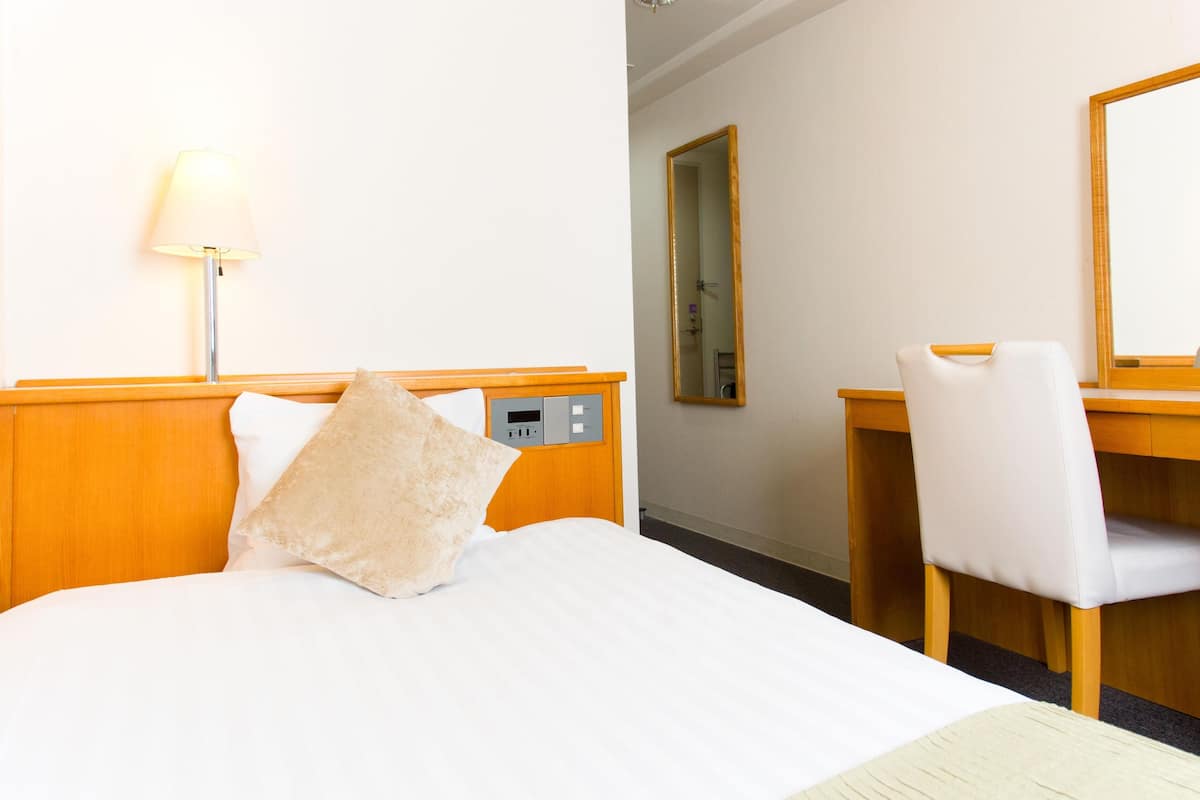 Une chambre d’hôtel avec un lit, un bureau, une chaise, une lampe et un miroir.