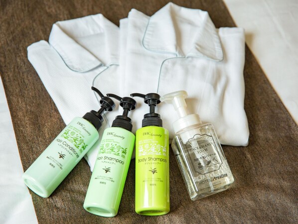 A set of toiletries including hair and body shampoo, a face and hand foam, and a bottle of clear liquid, arranged on a textured surface with a white cloth.