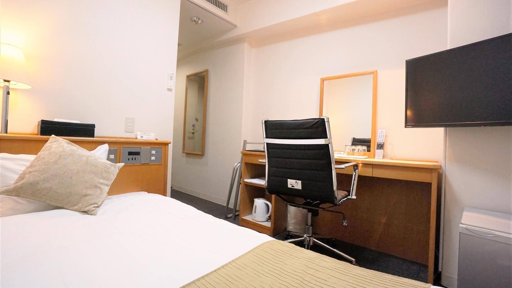 A hotel room with a bed, a desk, a chair, a television, and a coffee machine.