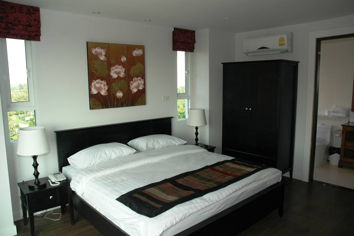 A bedroom with a large bed, two bedside tables with lamps, a wardrobe, and a painting on the wall.