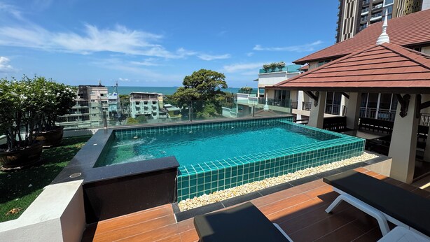 A rooftop swimming pool with a view of the sea, surrounded by buildings and greenery. - Jomtien Beach Penthouses (Pattaya)
