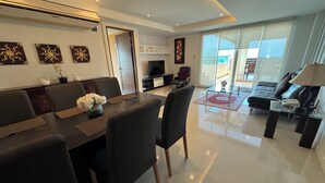 A modern living room with a dining area, a sofa, a TV, and a balcony with a view. - Jomtien Beach Penthouses (Pattaya)