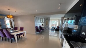 A modern kitchen with black appliances, a dining area with purple chairs, and a living room with a sofa and coffee table. - Jomtien Beach Penthouses (Pattaya)
