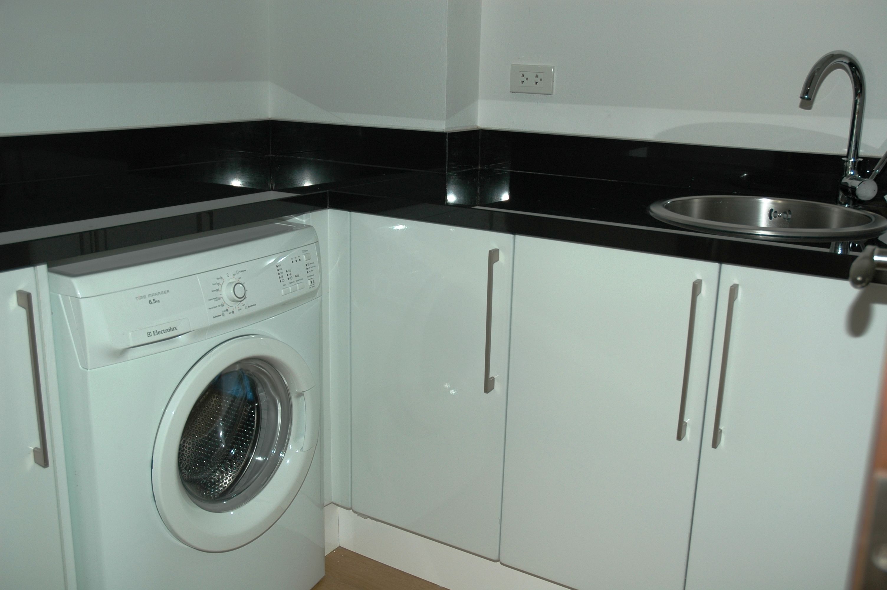 Une cuisine compacte équipée d’un lave-linge, d’un évier et de meubles blancs.