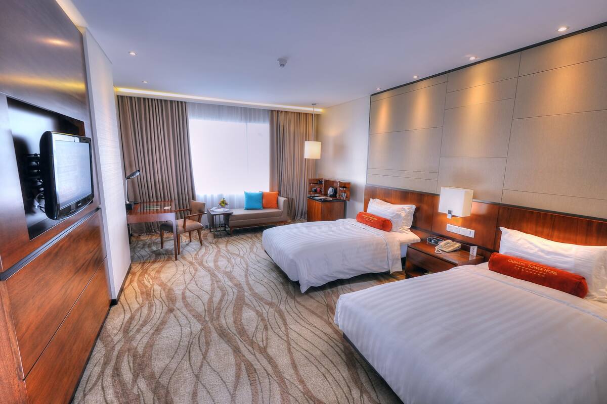 A hotel room with two beds, a desk, a TV, and a seating area with a view of the city.