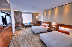 Une chambre d’hôtel avec deux lits, un bureau, une télévision et un coin salon offrant une vue sur la ville.