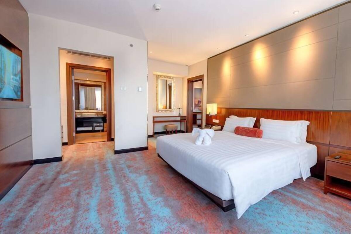 A hotel room with a large bed, a desk, a mirror, and a door leading to another room.
