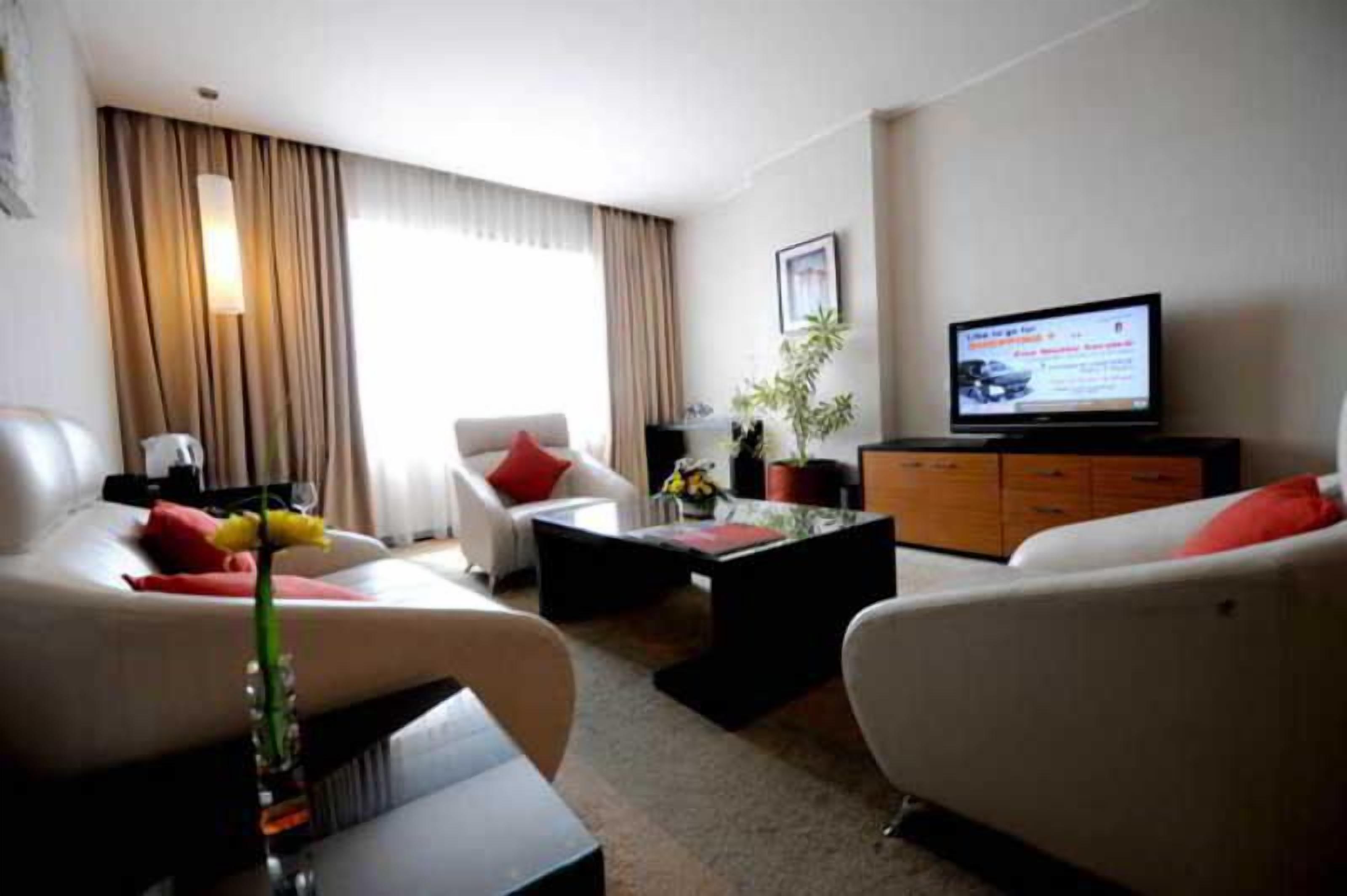 A hotel room with a sofa, armchair, coffee table, television, and a plant.