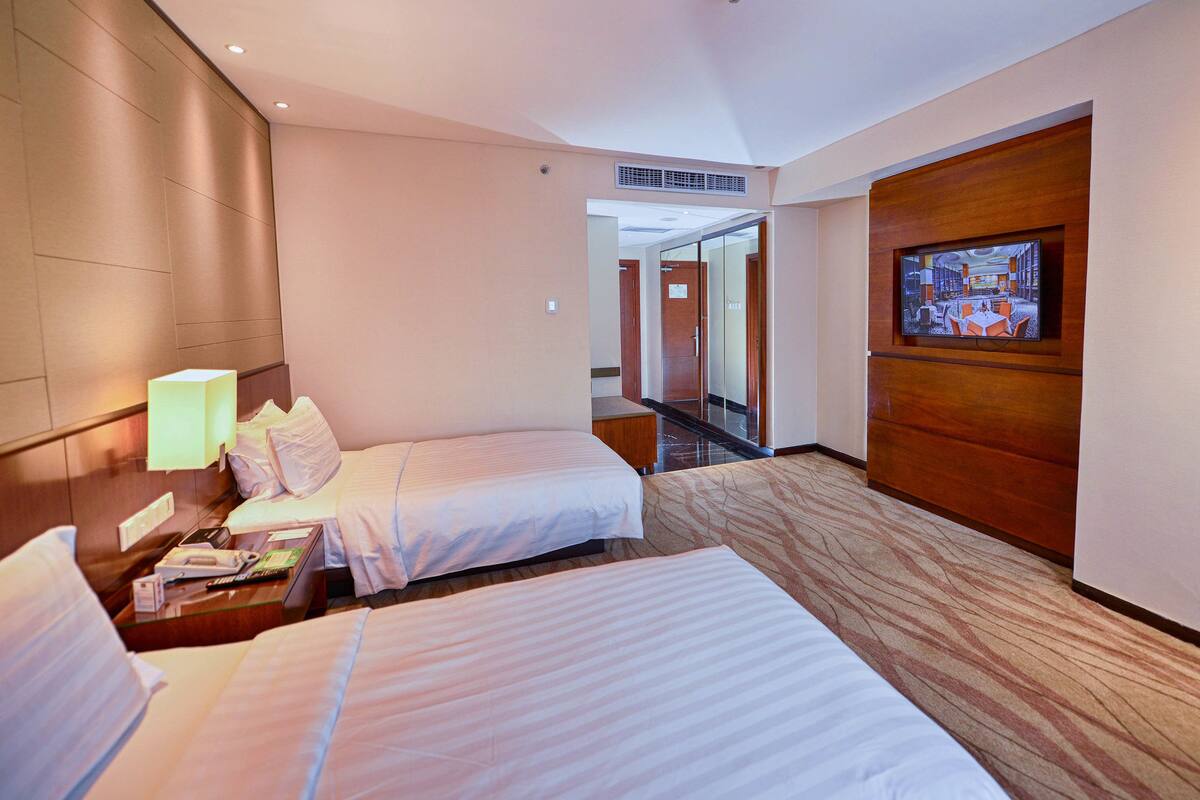 A hotel room with two beds, a television, and a desk with a lamp.