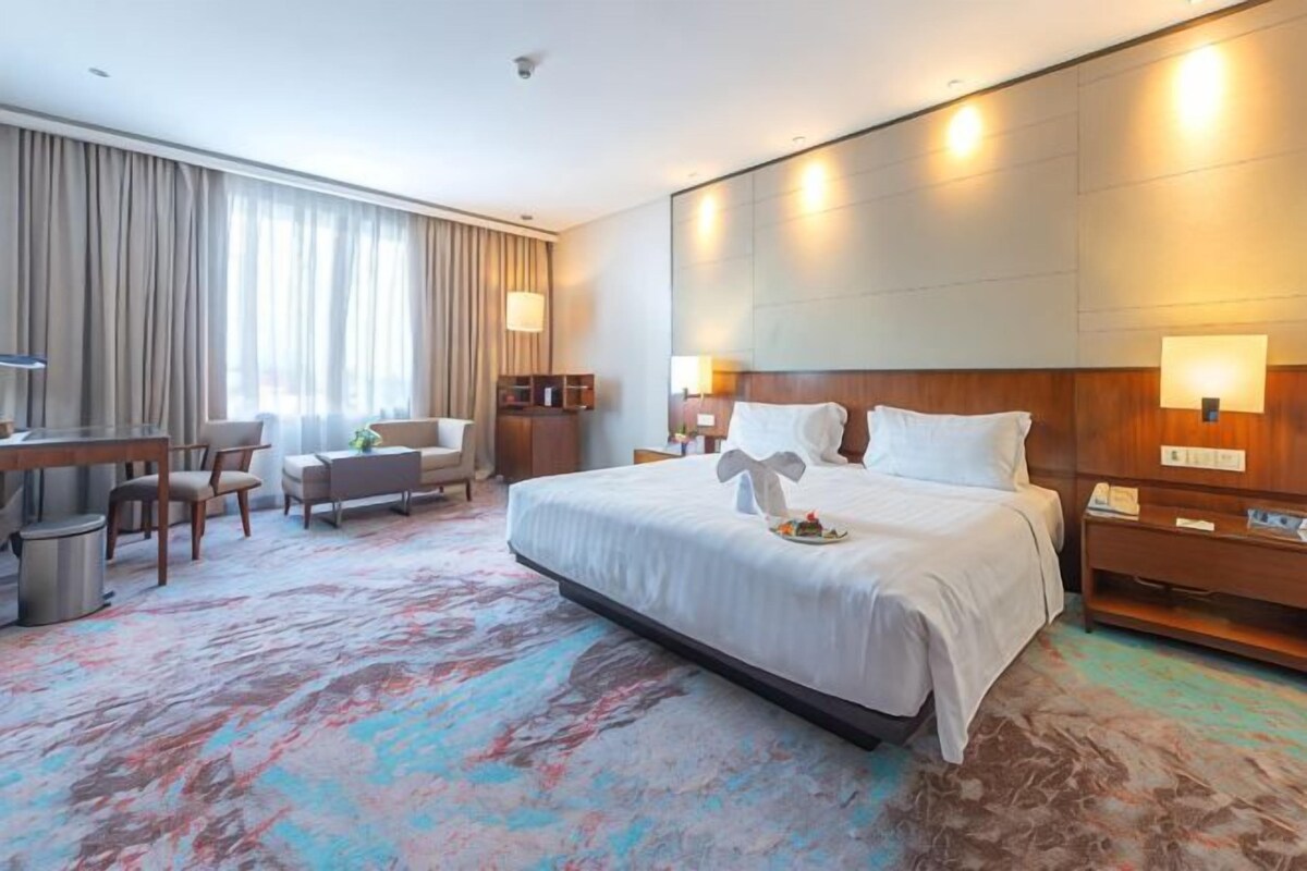 A hotel room with a large bed, a desk, a chair, a small table, and a TV.