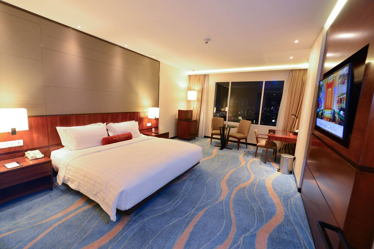 A hotel room with a large bed, a desk, a chair, a TV, and a window with a city view.