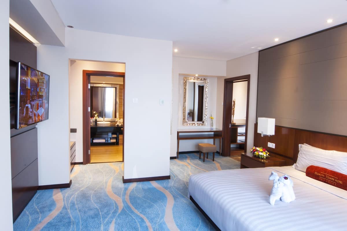 A hotel room with a large bed, a desk, a mirror, and a bathroom visible through an open door.