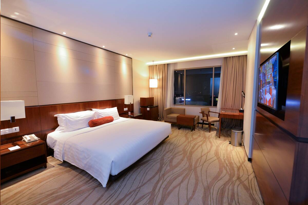 A hotel room with a large bed, a desk with a chair, a television, and a window with curtains.