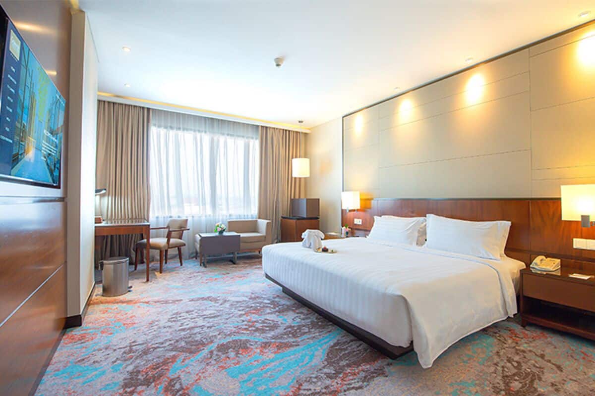 A hotel room with a large bed, a desk, a chair, a TV, and a window with curtains.