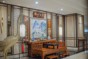 Un espace d’accueil de style chinois traditionnel, avec des meubles en bois, des œuvres de calligraphie et un tableau représentant des montagnes.